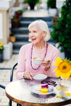 Beautiful and happy senior adult woman sitting at the bar cafeteria - Stylish fashionable old mature people relaxing in a modern cafe outdoorsの写真素材