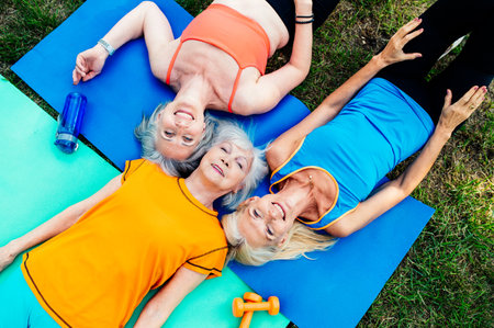 Group of beautiful sportive senior women training outdoors - Mature adults old friends doing fitness workout exercises in a park to stay healthy and fitの写真素材