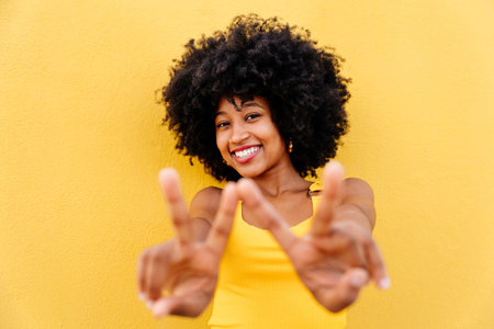 Beautiful young happy african woman with afro curly hairstyle strolling in the city - Cheerful black student portrait on colorful wall backgroundの写真素材
