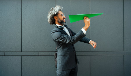Cinematic and storytelling image of a young entrepreneur throwing a green paper aircraft in the air. Conceptual representation of green energy and technology ideasの写真素材