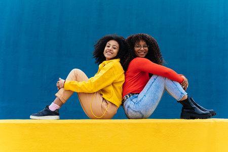 Young happy women posing on colored blue and yellow colored walls. Teenagers girl spending time together after schoolの写真素材