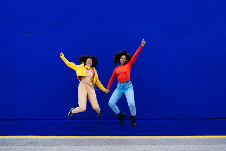 Young happy women dancing and having fun outdoors. Teenagers listening to music with smartphones and headphones in a yellow and blue modern urban areaの写真素材