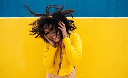 Young happy woman dancing and having fun outdoors. Teenager listening to music with smartphone and headphones in a yellow and blue modern urban areaの写真素材