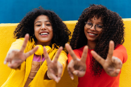 Young happy women dancing and having fun outdoors. Teenagers listening to music with smartphones and headphones in a yellow and blue modern urban areaの写真素材