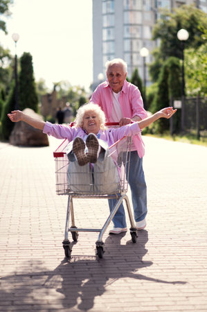 Old modern couple dressing fashionable colored clothes. Youthful grandmother and grandfather having fun outdoor and going wild. Representation of elderly people feeling young insideの写真素材