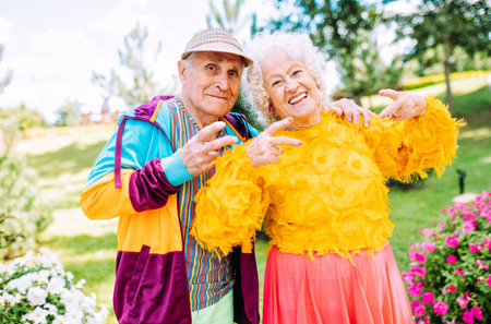 Old modern couple dressing fashionable colored clothes. Youthful grandmother and grandfather having fun outdoor and going wild. Representation of elderly people feeling young insideの写真素材