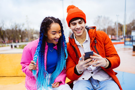 Multiracial young couple of lovers dating outdoors in winter using social media app on smartphone,...