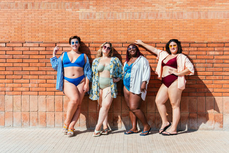 Group of beautiful plus size women with swimwear bonding and having fun at the beach, posing on a brick wall background - Curvy female friends enjoying summertime at the sea, concepts about body acceptance, body positive and self confidenceの写真素材