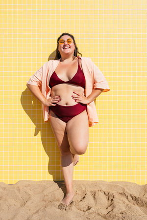 Beautiful and confident plus size woman having fun at the beach, posing on colorful wall background - concepts about body acceptance, body positive, self confidence and body careの写真素材
