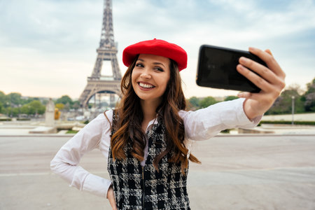 Beautiful young woman visiting paris and the eiffel tower. Parisian girl with red hat and fashionable clothes having fun in the city center and landmarks areaの写真素材