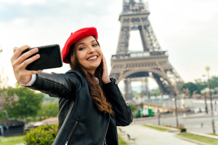 Beautiful young woman visiting paris and the eiffel tower. Parisian girl with red hat and fashionable clothes having fun in the city center and landmarks areaの写真素材