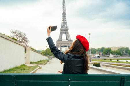 Beautiful young woman visiting paris and the eiffel tower. Parisian girl with red hat and fashionable clothes having fun in the city center and landmarks areaの写真素材