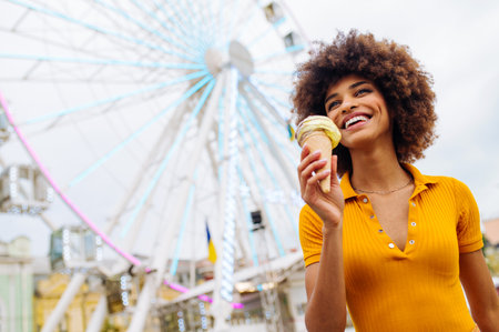Beautiful young black woman eating ice cream at amusement park - Cheerful african-american female portrait during summertime vacation- Leisure, people and lifestyle conceptsの写真素材