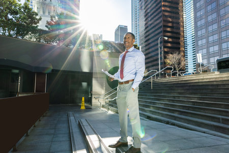 Handsome male african american business man CEO in a stylish corporate elegant suit in a business center outdoors - Black male commuter going to work, city and financial district in the backgroundの写真素材