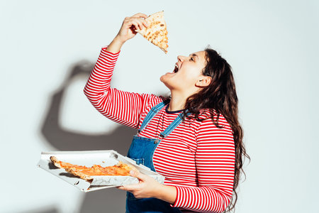 Plus size woman model posing in studio and having fun. Eating italian pizza from the boxの写真素材