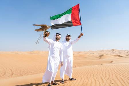Two middle-eastern men wearing traditional emirati arab kandura bonding in the desert and holding a...