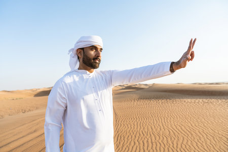 Handsome and successful middle-eastern man wearing traditional emirati arab kandura in the desert -...