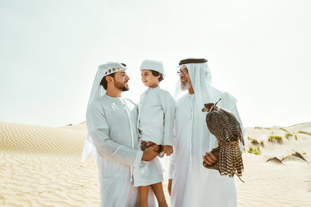 Three generation family making a safari in the desert of Dubai. Grandfather, son and grandson spending time together in the nature and training their falcon bird.の写真素材