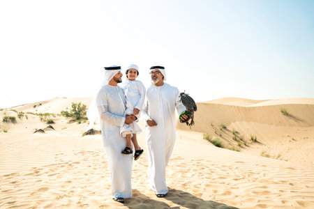 Three generation family making a safari in the desert of Dubai. Grandfather, son and grandson spending time together in the nature and training their falcon bird.の写真素材
