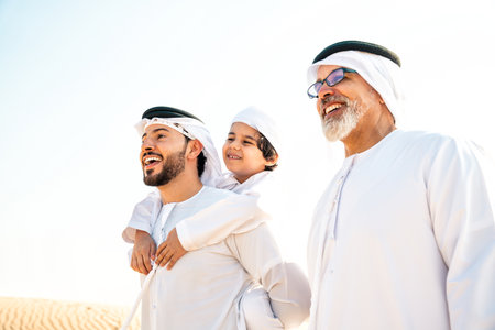 Three generation family making a safari in the desert of Dubai wearing white kandura outfit. Grandfather, son and grandson spending time together in the nature.の写真素材