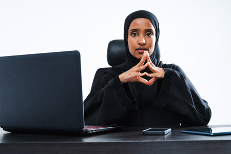 Beautiful arab middle-eastern corporate businesswoman with traditional abaya dress working in the office- Arabic muslim adult female portrait at computer desk in Dubai, United Arab Emiratesの写真素材
