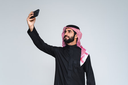 Handsome arab middle-eastern saudi arabian man with traditional saudi clothing in studio - Arabic muslim adult male businessman wearing thwab portrait isolated on gray backgroundの写真素材