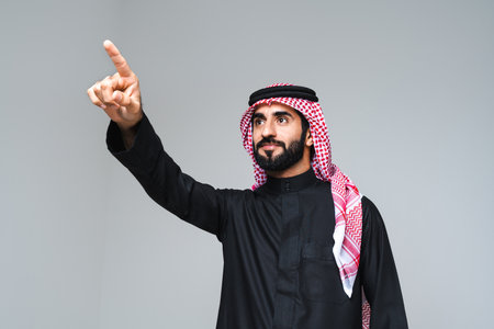 Handsome arab middle-eastern man with traditional saudi clothing in studio - Arabic muslim adult male businessman wearing thwab portrait isolated on gray backgroundの写真素材