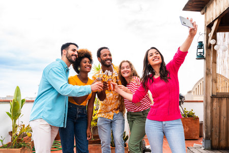 Multiethnic group of happy young friends having dinner barbecue party on rooftop at home - Multiracial cheerful young adult people having fun and bonding on a terrace balcony with city view, eating and drinking.の写真素材