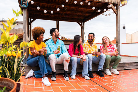 Multiethnic group of happy young friends having dinner barbecue party on rooftop at home - Multiracial cheerful young adult people having fun and bonding on a terrace balcony with city view, eating and drinking.の写真素材