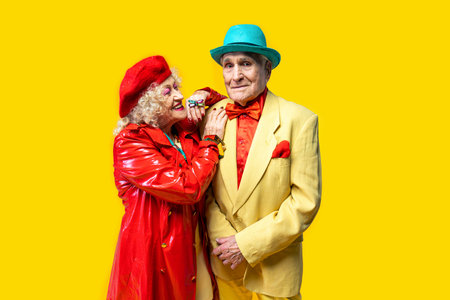Beautiful senior old couple wearing fancy party clothes acting in studio on a colored background....