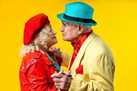 Beautiful senior old couple wearing fancy party clothes acting in studio on a colored background....