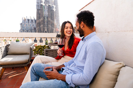 Multiracial beautiful happy couple of lovers dating on rooftop balcony at Sagrada Familia, Barcelona - Multiethnic people having romantic aperitif on a terrace with city view, concepts about tourism and people lifestyleの写真素材