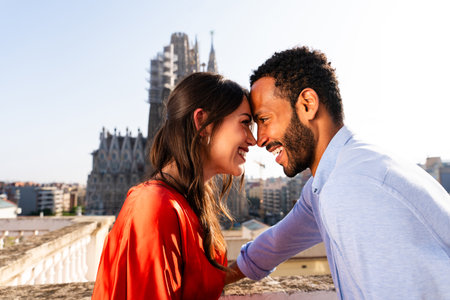 Multiracial beautiful happy couple of lovers dating on rooftop balcony at Sagrada Familia, Barcelona - Multiethnic people having romantic meeting on a terrace with city view, concepts about tourism and people lifestyleの写真素材