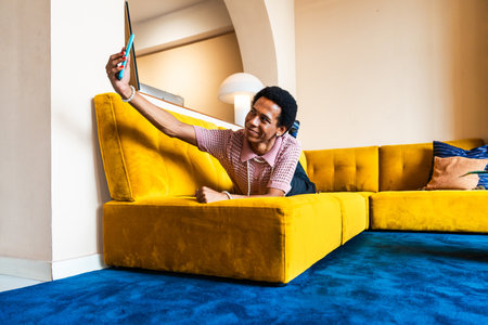 Fluid gender young man wearing cross dressing clothing at home, LGBTQ and diversity concepts - Hispanic non binary male portrait in a colorful apartment, LGBT people conceptsの写真素材