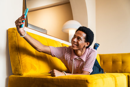 Fluid gender young man wearing cross dressing clothing at home, LGBTQ and diversity concepts - Hispanic non binary male portrait in a colorful apartment, LGBT people conceptsの写真素材