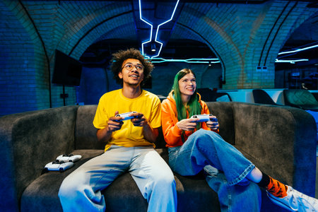 Multiethnic group of young friends playing videogames at home sitting on the sofa - Videogamers...