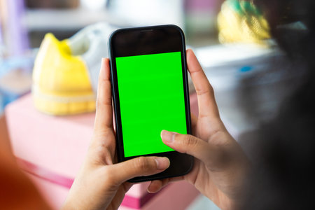 Beautiful young hispanic woman managing her home clothing e-commerce business from home - Online shopping store, close-up on mobile phone green screen - concept of home businessの写真素材