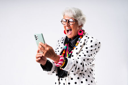 Beautiful senior woman with gray hair wearing colorful stylish clothing portrait in studio - Cheerful old grandmother with fashionable style holding mobile phoneの写真素材