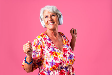 Beautiful senior woman with gray hair wearing colorful stylish clothing portrait in studio - Cheerful old grandmother with fashionable style dancing while listening to musicの写真素材