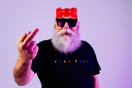 Senior old man with gray beard doing rude rebel gesture, portrait in studio - Funny stylish older...