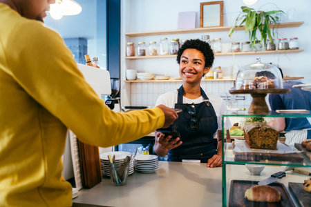 Bakery, happy portrait of black woman in cafe ready for serving pastry, coffee and baked foods. Restaurant, coffee shop and confident waiter barista by counter for service, help and welcomeの写真素材