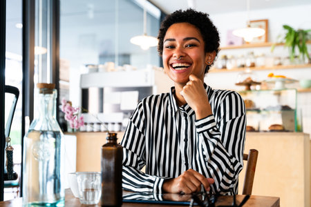 Beautiful young african woman with short hair sitting in a bar cafeteria - Pretty cheerful african-american female relaxing in a pastry bakery coffee shopの写真素材