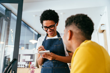 Bakery, happy portrait of black woman in cafe ready for serving pastry, coffee and baked foods. Restaurant, coffee shop and confident waiter barista by counter for service, help and welcomeの写真素材