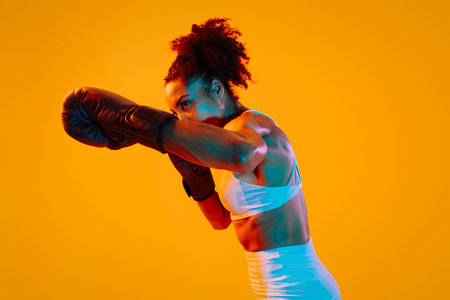 Sportive black hispanic woman wearing sportswear training in fitness studio, colorful dramatic lighting - African-american female athlete doing sport workoutの写真素材