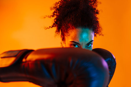 Sportive black hispanic woman wearing sportswear training in fitness studio, colorful dramatic lighting - African-american female athlete doing sport workoutの写真素材