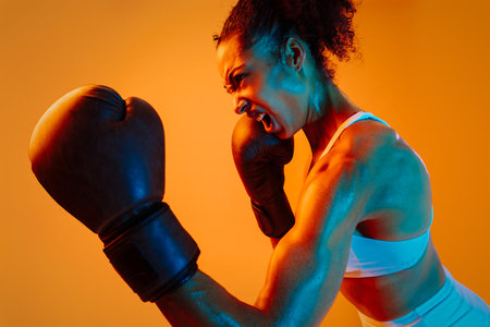 Sportive black hispanic woman wearing sportswear training in fitness studio, colorful dramatic lighting - African-american female athlete doing sport workoutの写真素材
