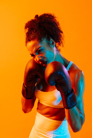 Sportive black hispanic woman wearing sportswear training in fitness studio, colorful dramatic lighting - African-american female athlete doing sport workoutの写真素材