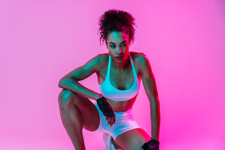 Sportive black hispanic woman wearing sportswear training in fitness studio, colorful dramatic lighting - African-american female athlete doing sport workoutの写真素材
