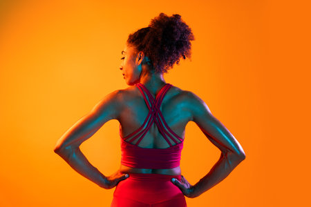 Sportive black hispanic woman wearing sportswear training in fitness studio, colorful dramatic lighting - African-american female athlete doing sport workoutの写真素材