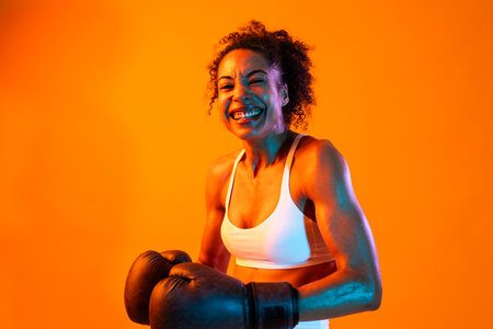 Sportive black hispanic woman wearing sportswear training in fitness studio, colorful dramatic...